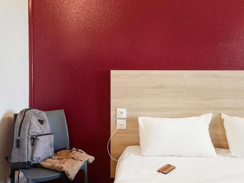 a bed with a backpack next to a red wall at hotelF1 Genève Aéroport Ferney in Ferney-Voltaire