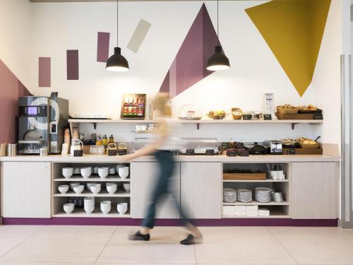 a woman walking past a counter in a coffee shop at Aparthotel Adagio access München City Olympiapark in Munich