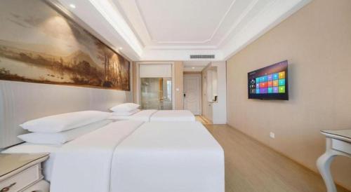 a bedroom with a white bed and a painting on the wall at Vienna Hotel Guiyang Jiaxiulou Jichang Road in Guiyang