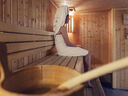 a woman sitting on a bench in a sauna at Mercure Maurepas Saint Quentin in Maurepas