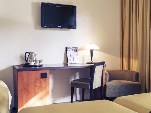 a hotel room with a desk with a tv and a chair at Mercure Maurepas Saint Quentin in Maurepas