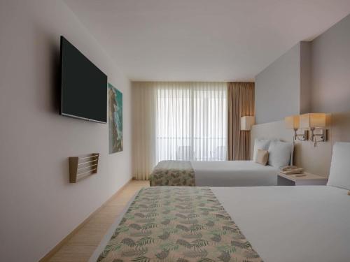 a hotel room with two beds and a flat screen tv at Mercure Santa Marta Emile in Santa Marta