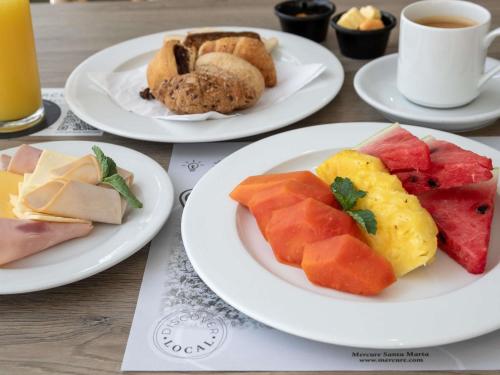 three plates of food on a table with plates of fruit at Mercure Santa Marta Emile in Santa Marta