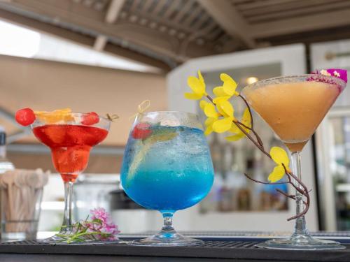 three cocktails sitting on a table with flowers on it at Mercure Santa Marta Emile in Santa Marta
