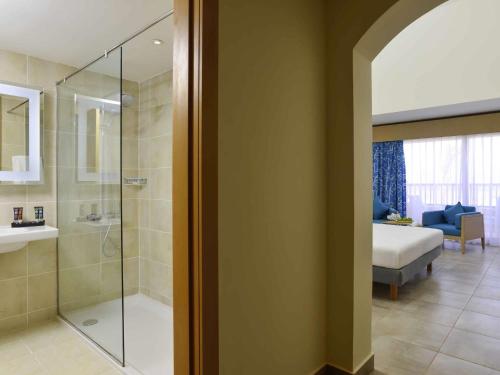 a bathroom with a glass shower and a bedroom at Novotel Marsa Alam Beach Resort in Quseir