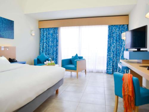 a hotel room with a bed and two blue chairs at Novotel Marsa Alam Beach Resort in Quseir