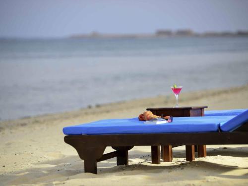a picnic table on the beach with a drink on it at Novotel Marsa Alam Beach Resort in Quseir