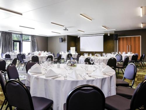 a conference room with white tables and chairs and a screen at Novotel New Plymouth Taranaki in New Plymouth