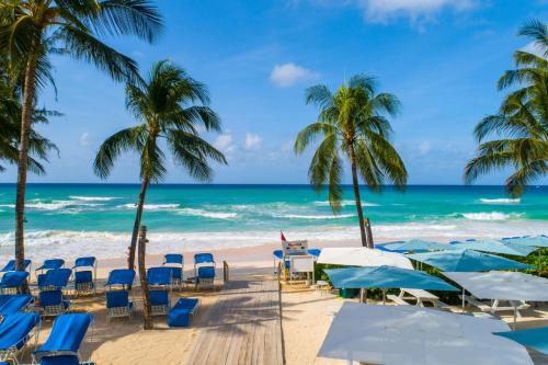 a beach with chairs and palm trees and the ocean at Turtle Beach, a Tribute Portfolio All Inclusive Hotel in Christ Church