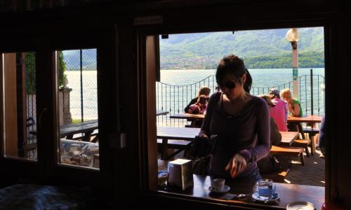 a woman sitting at a table looking out a window at Camping Villaggio Paradiso in Domaso