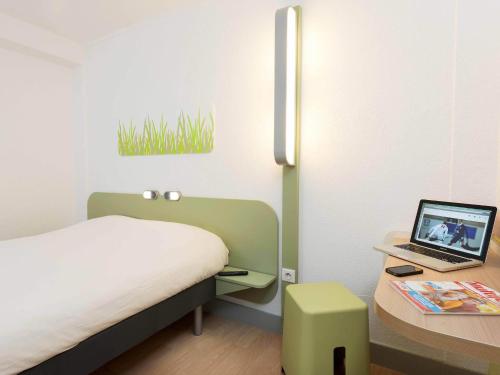 a bedroom with a bed and a laptop on a table at Ibis Budget Béziers Est La Giniesse in Béziers