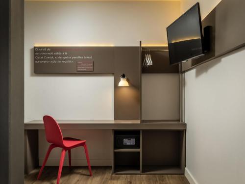 a red chair sitting next to a desk with a tv at ibis Styles Barcelona Centre in Barcelona