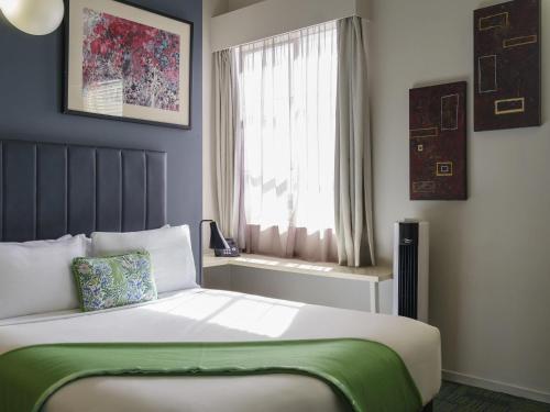 a bedroom with a bed with a green blanket and a window at Ibis Styles Invercargill in Invercargill