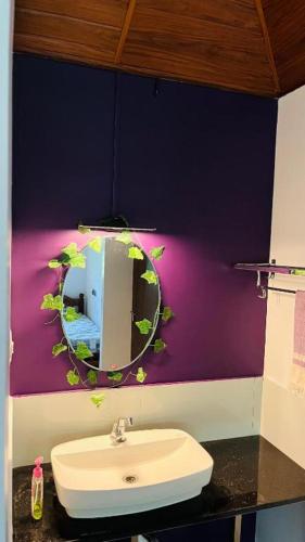 Un baño con un lavabo y un espejo en una pared morada. en CatsClaw Inn, en Talayolaparambu