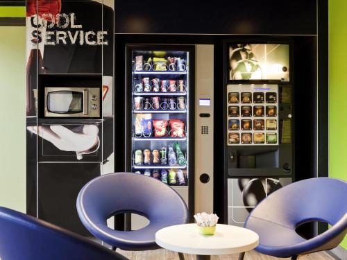 a restaurant with two blue chairs and a refrigerator at ibis budget Pontault Combault RN4 Marne La Vallée in Pontault-Combault