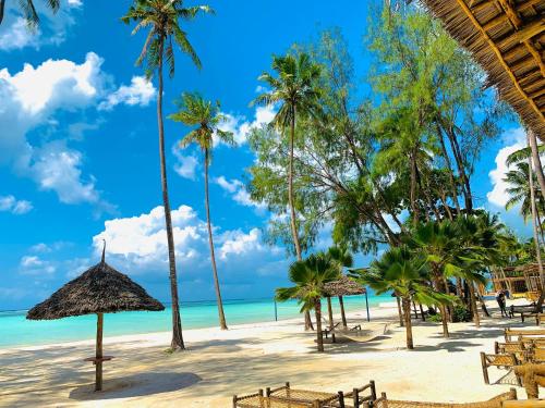 a beach with chairs and palm trees and the ocean at Royal Mandarin Hotel & Resort in Pwani Mchangani