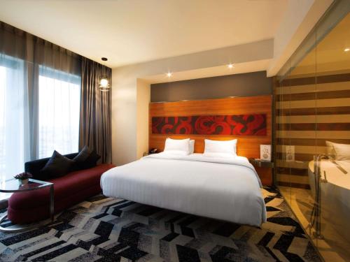 a bedroom with a large white bed and a red couch at Novotel Pekanbaru in Pekanbaru