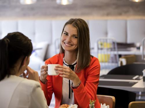 a woman smiling while holding a cup of coffee at Novotel Wrocław Centrum in Wrocław
