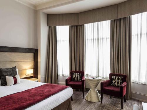 a hotel room with a bed and two chairs and a table at Mercure Aberdeen Caledonian Hotel in Aberdeen