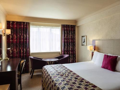 a hotel room with a bed and a desk and a window at Mercure Daventry Court Hotel in Daventry