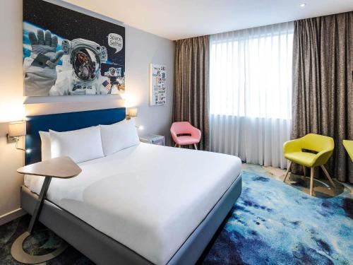 a hotel room with a large bed and a yellow chair at ibis Styles London Heathrow Airport in Hillingdon
