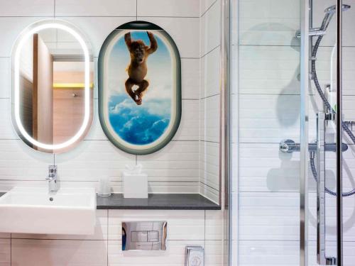 a bathroom with a monkey jumping in a mirror at ibis Styles London Heathrow Airport in Hillingdon
