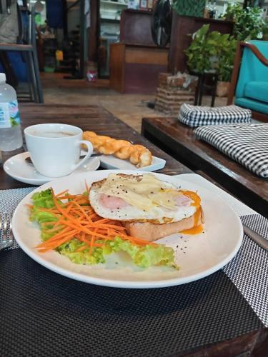 a plate with a sandwich and carrots and a cup of coffee at Laanrablom Bed&Breakfast in Sara Buri