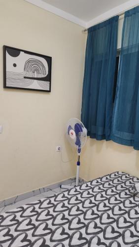 a room with a bed with a fan and blue curtains at NO CASH ACCEPTED-MEETING POINT-Volcanic Beach Refuge-Group Housing in São Filipe