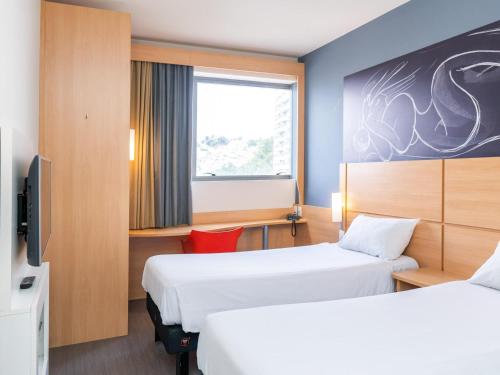 a hotel room with two beds and a window at ibis Santos Valongo in Santos