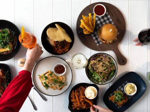 a table with plates of food and a person holding a drink at ibis Styles Brisbane Elizabeth Street in Brisbane