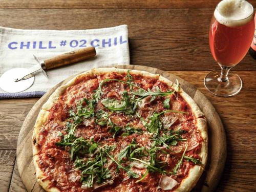 a pizza on a table next to a glass of beer at ibis Cambridge Central Station in Cambridge