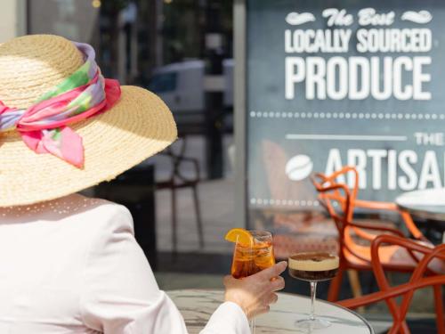 a woman in a straw hat sitting at a table with a drink at ibis Cambridge Central Station in Cambridge