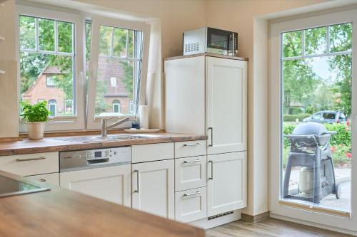 a kitchen with white cabinets and a sink and windows at Villa Kanalblick, Schiffsdeck in Oldenbüttel