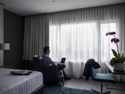 a man sitting in a chair with a laptop in a hotel room at Pullman Miri Waterfront in Miri