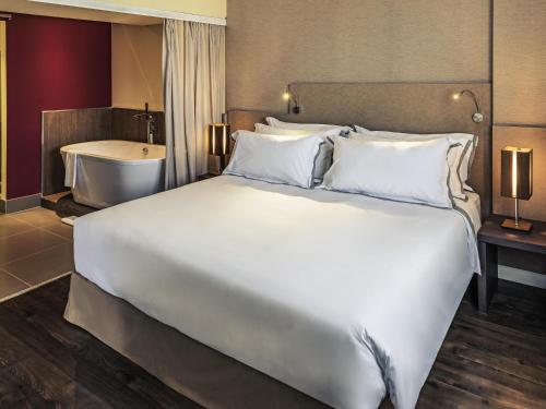 a large white bed in a hotel room with a tub at Mercure Ribeirao Preto in Ribeirão Preto