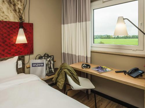a hotel room with a bed and a desk and a window at Ibis München Airport Süd in Hallbergmoos