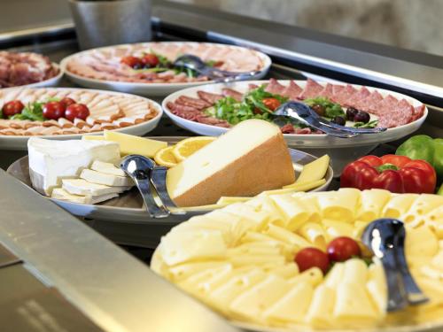 a buffet filled with different types of cheese and vegetables at Ibis München Airport Süd in Hallbergmoos