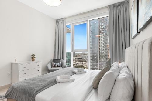 a bedroom with a white bed with a large window at Stylish 1BR in Wasl 1 with Balcony & Pool in Dubai