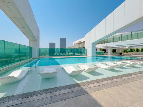 a large building with a swimming pool with white chairs at Stylish 1BR in Wasl 1 with Balcony & Pool in Dubai