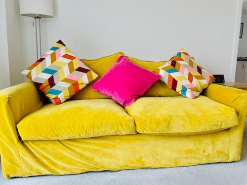 ein gelbes Sofa mit zwei bunten Kissen darauf in der Unterkunft Stunning Modern Four Bed Home Near Witney & Oxford in Oxford