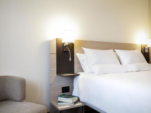 a bedroom with a bed with a lamp and a chair at Novotel Brescia Due in Brescia