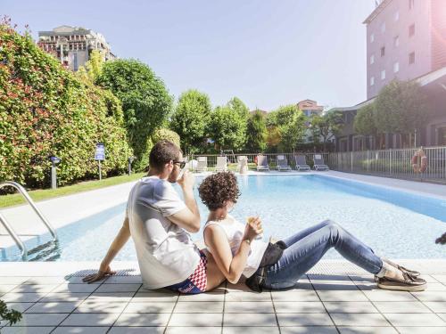 a man and a woman sitting next to a pool at Novotel Brescia Due in Brescia