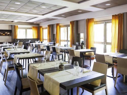a dining room with tables and chairs and windows at Novotel Brescia Due in Brescia