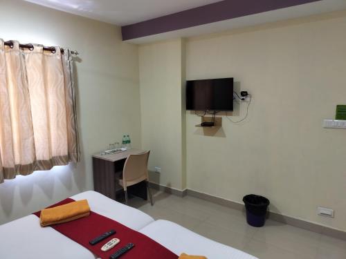 een slaapkamer met een bed, een bureau en een tv bij VRJ Residency inn in Chennai
