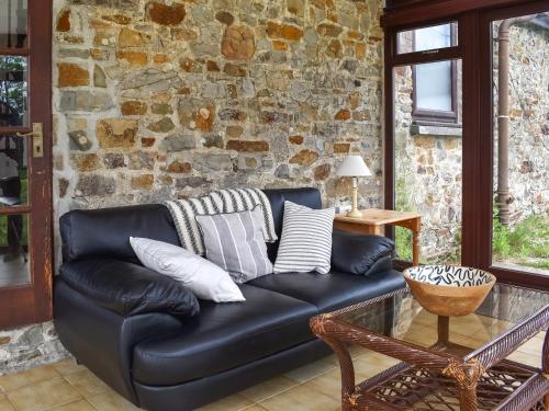 ein schwarzes Ledersofa vor einer Steinmauer in der Unterkunft Crooklets Cottage in Bude