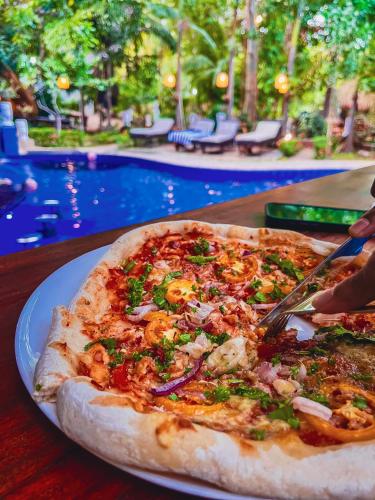 a pizza on a plate on a table next to a pool at Sundaras Resort LTD in Dambulla