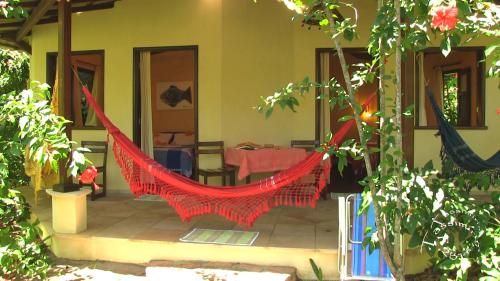 a red hammock in a house with a table at Pousada Tassimirim in Ilha de Boipeba