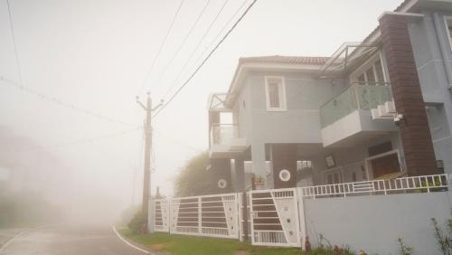 a foggy street next to a house with a white fence at Aruvi Homestay in Kodaikānāl