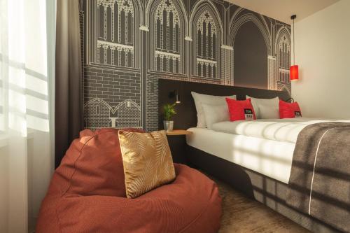 a bedroom with a bed and a chair at Holiday Inn - the niu, Sparrow Regensburg by IHG in Regensburg
