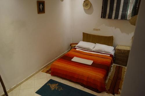 a small bedroom with a bed with a colorful blanket at Bright Wave Surfhouse in Tamraght Ouzdar